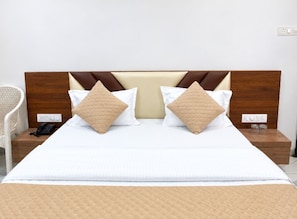 A neatly made bed with two pillows, a bedside table with a phone, and a wall socket. - Hotel Shreedha Palace (Indore)