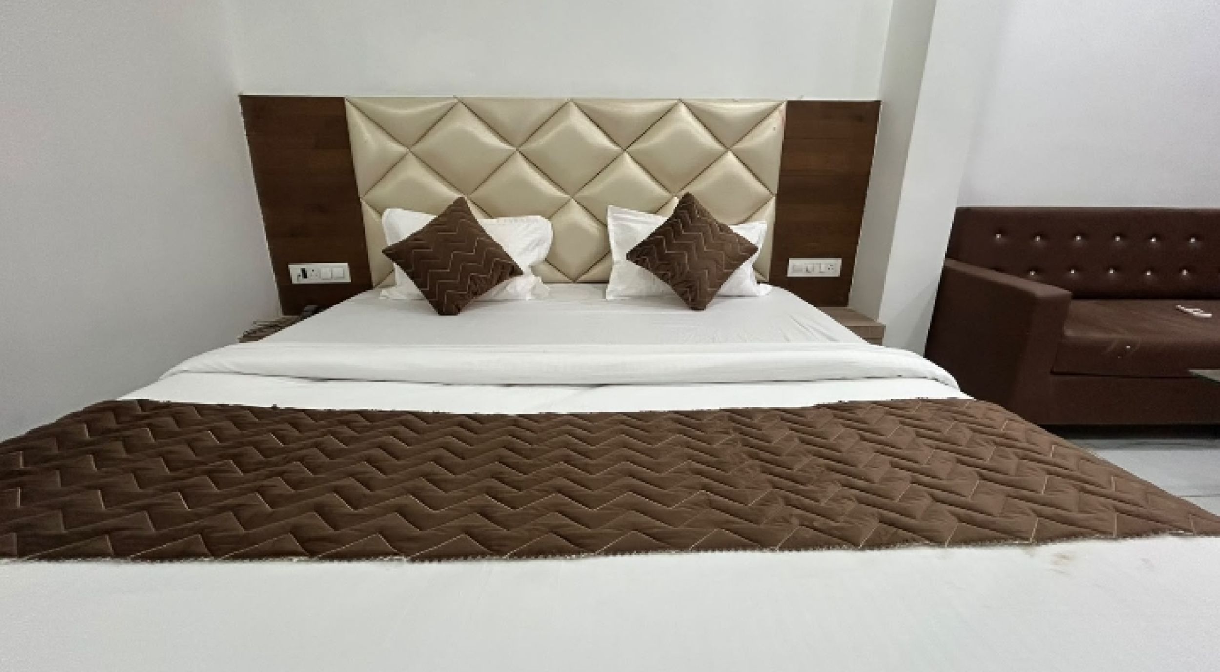 Una cama con cabecera acolchada, dos almohadas y una manta marrón.