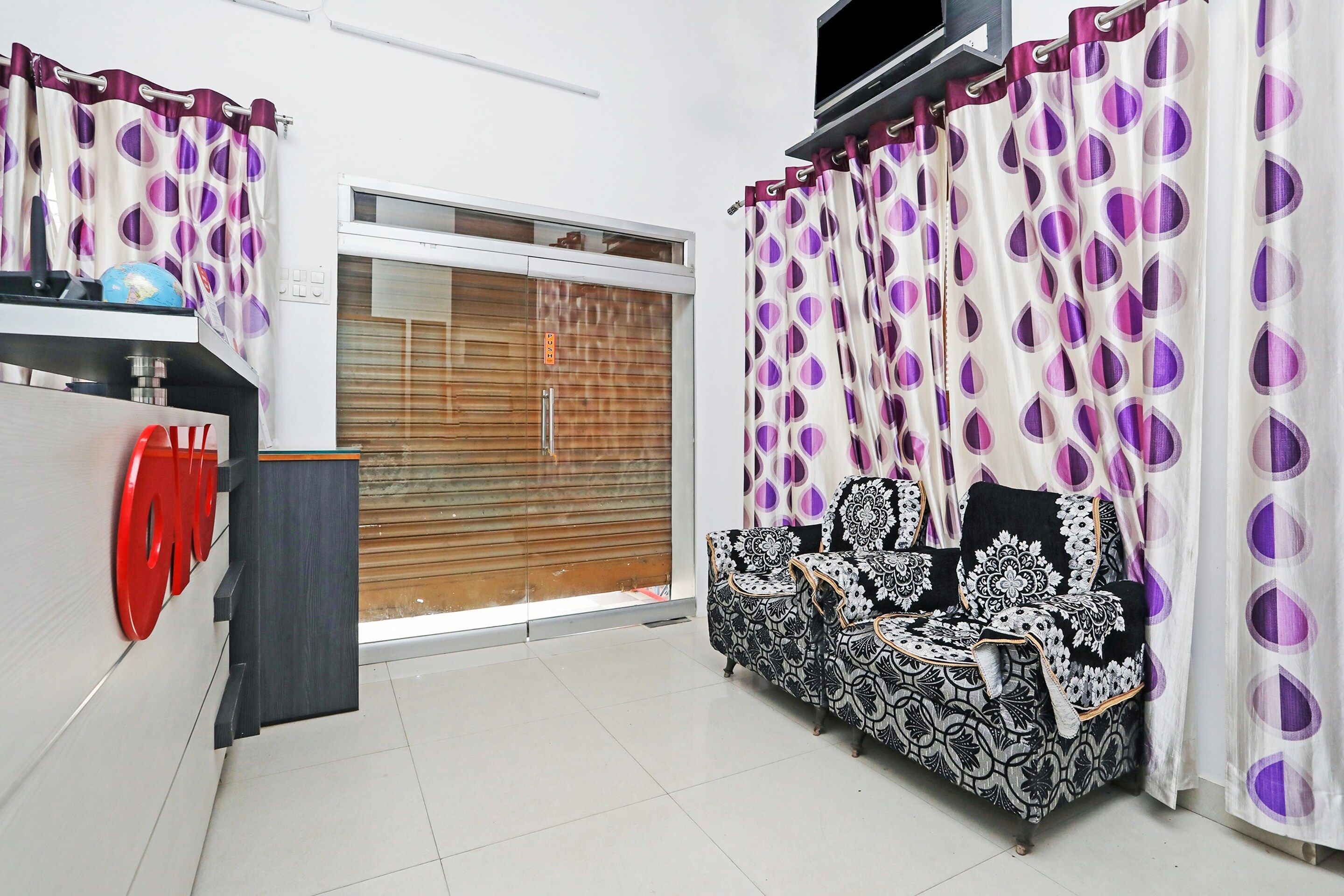A room with a sofa, a television, and a window with curtains.