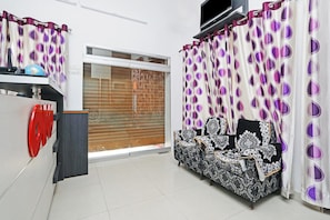 Una habitación con sofá, televisión y ventana con cortinas.
