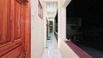 A corridor with a wooden door on the left, a marble floor, and a view of the outside at night.