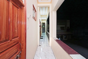 Un pasillo con una puerta de madera a la izquierda, suelo de mármol y vista al exterior de noche.