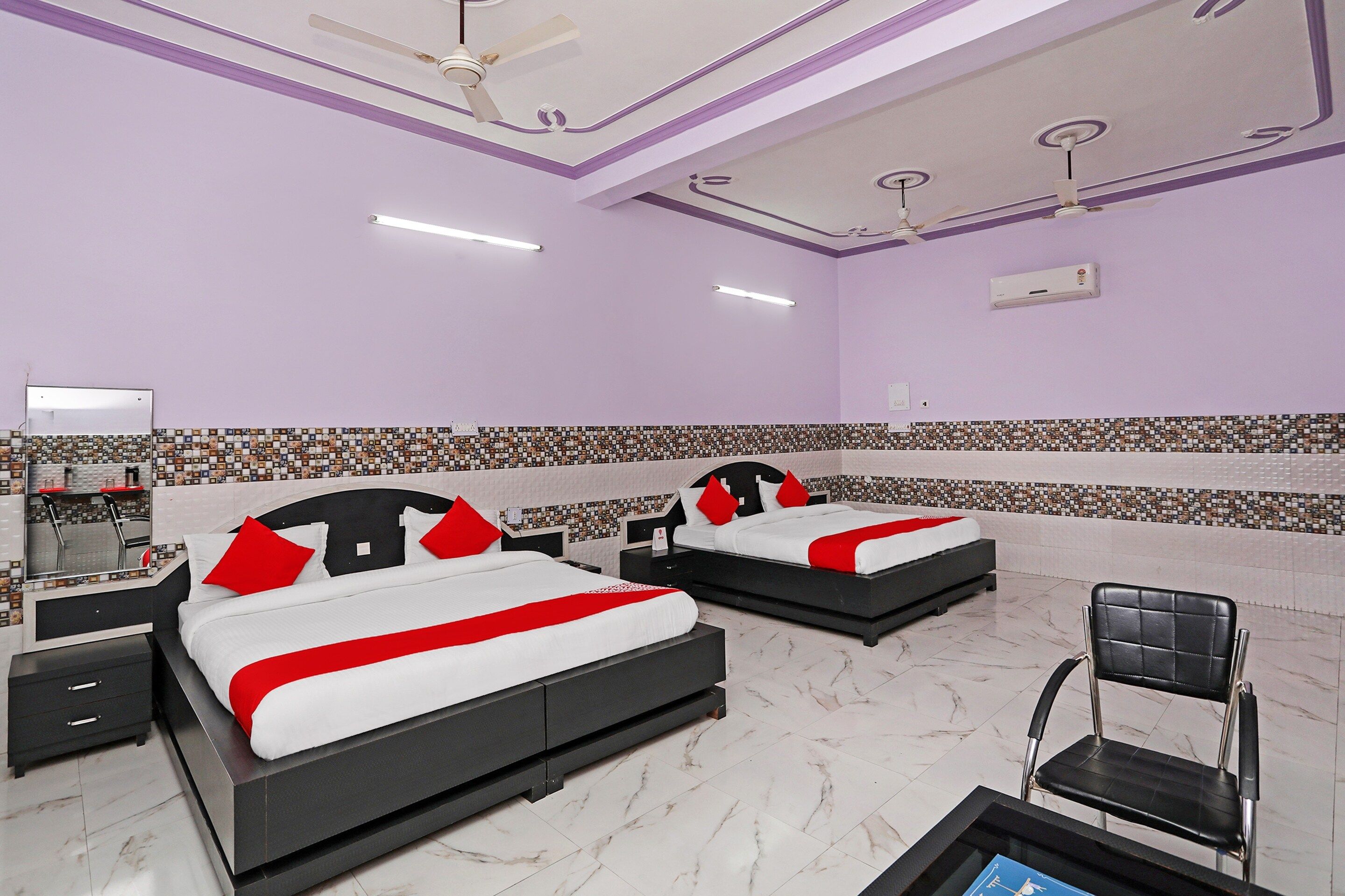 A hotel room with two beds, a chair, a desk, and a ceiling fan.
