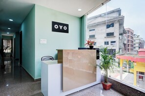 Un comptoir d'accueil avec une enseigne indiquant « OYO », situé dans le hall d'un hôtel, d'où l'on peut voir les bâtiments environnants.
