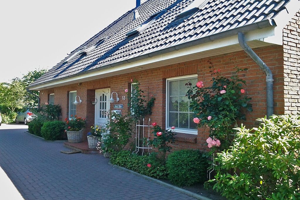 A brick house with a tiled roof, a front porch with a white door, and a garden with pink roses.