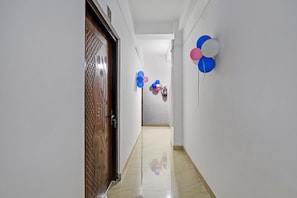 Un pasillo con puerta de madera, paredes blancas y suelo de baldosas.