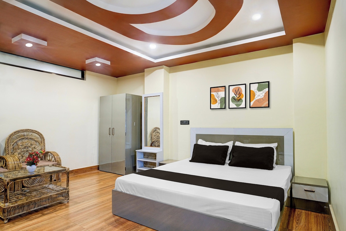 Une chambre à coucher moderne avec un grand lit, une armoire, un coin salon avec une table et des œuvres d’art accrochées au mur.