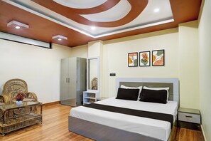 Une chambre à coucher moderne avec un grand lit, une armoire, un coin salon avec une table et des œuvres d’art accrochées au mur.