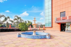 A fountain with a tiered design in a courtyard with patterned paving, surrounded by a building with large windows and a balcony. - Hotel O Jyoti Guest House (Guwahati)
