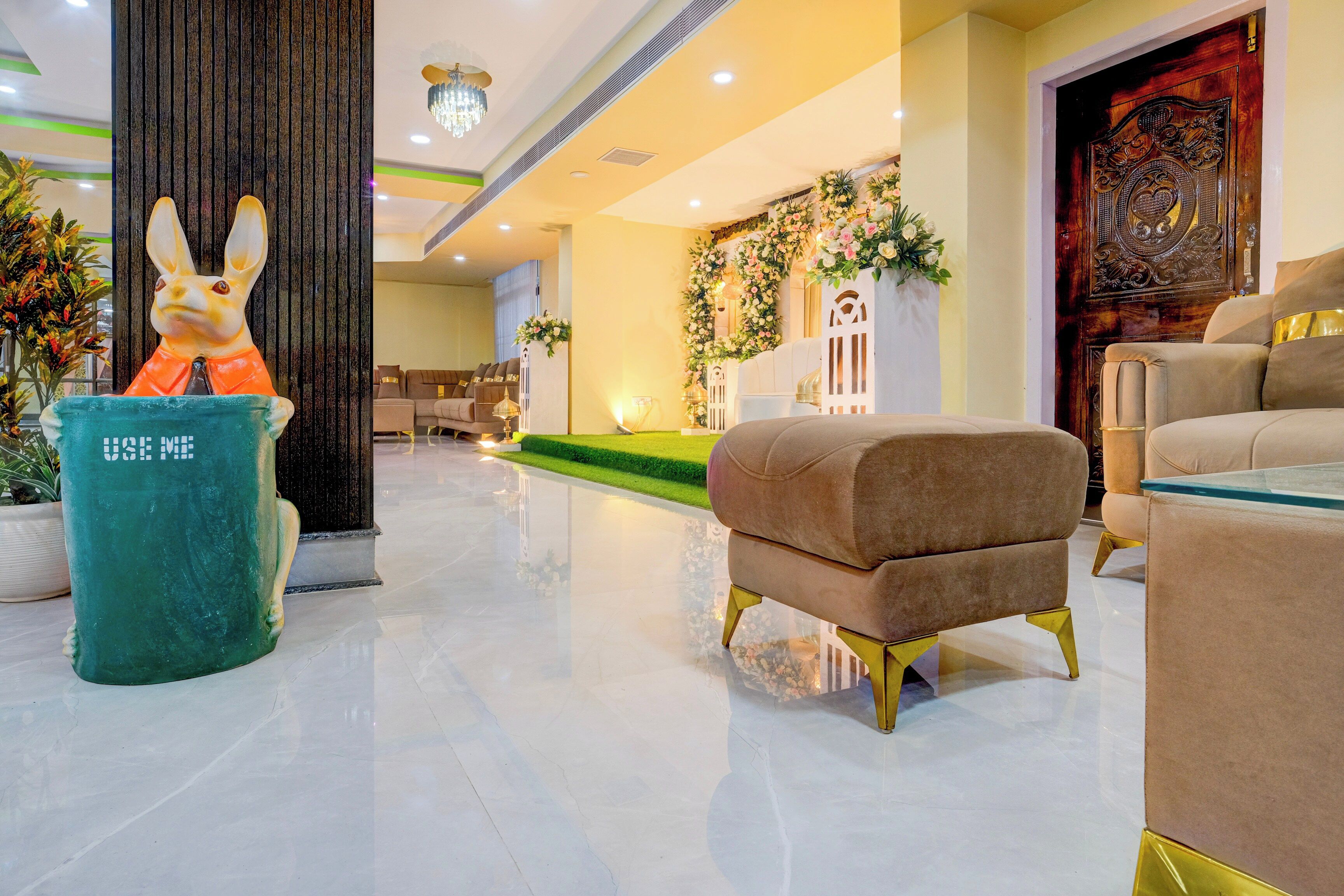 A lobby with a green trash bin, a plush armchair, and a decorative wall with floral arrangements.