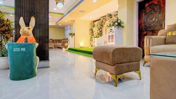 A lobby with a green trash bin, a plush armchair, and a decorative wall with floral arrangements.