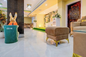 A lobby with a green trash bin, a plush armchair, and a decorative wall with floral arrangements. - Hotel O Jyoti Guest House (Guwahati)