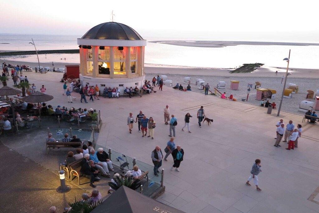 A public square with a central gazebo, seating areas, and a beach in the background.
