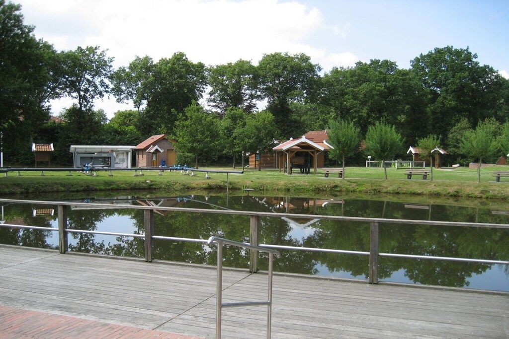 Un parc avec une terrasse en bois, un petit bâtiment et un étang.
