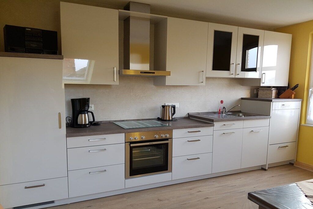 A modern kitchen with white cabinetry, a built-in oven, and a coffee maker.