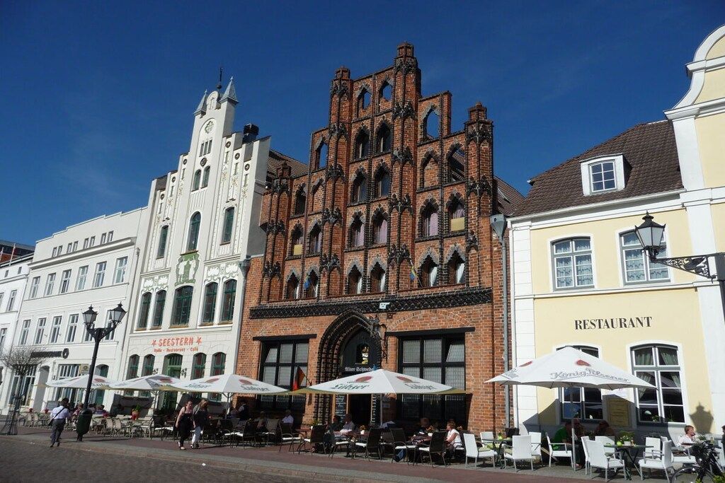 A historic building with a clock tower, a restaurant, and outdoor seating with umbrellas.