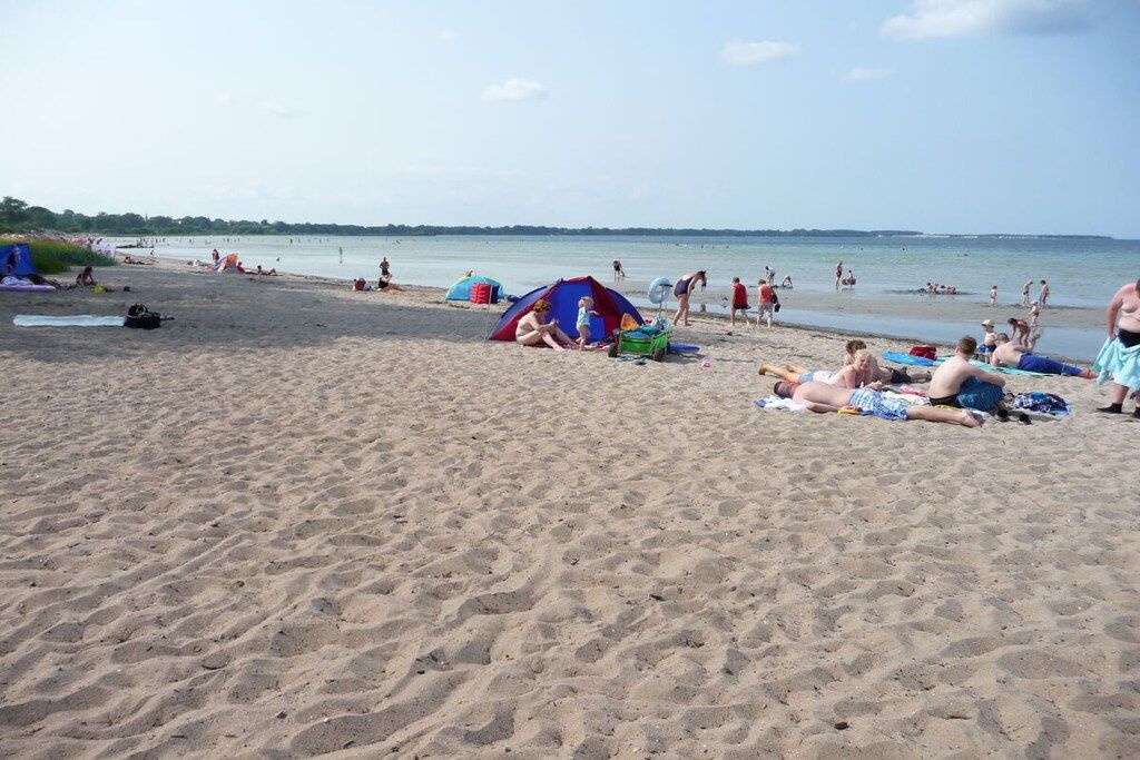 A beach with people sunbathing and swimming, tents, and a clear sky.