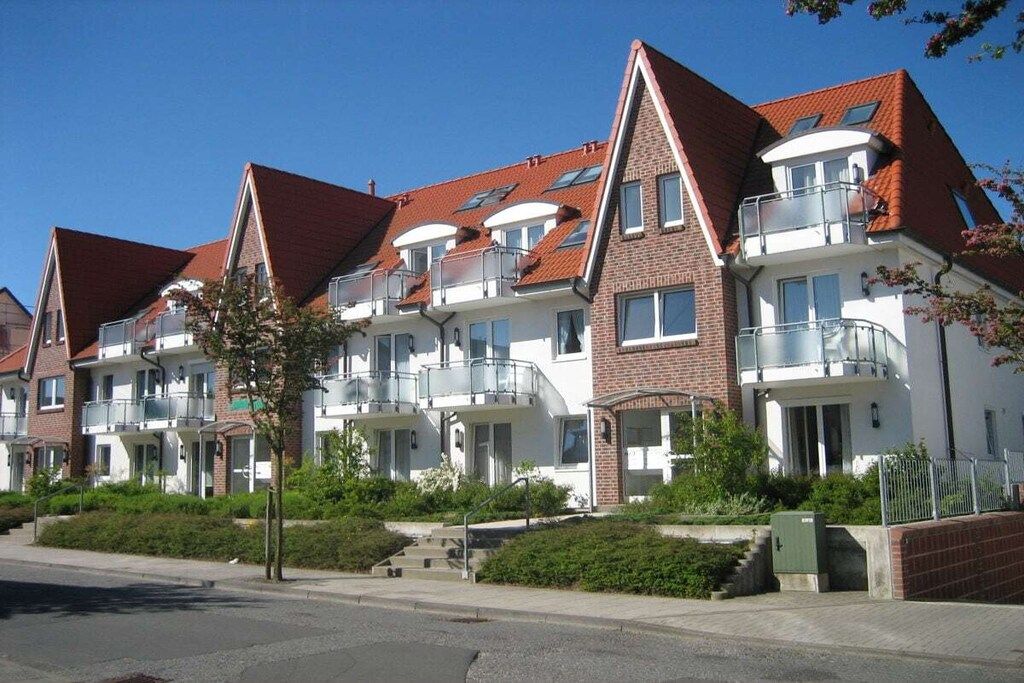 Eine Reihe moderner Apartmenthäuser mit Balkonen, blauem Himmel und einem gepflegten Rasen.