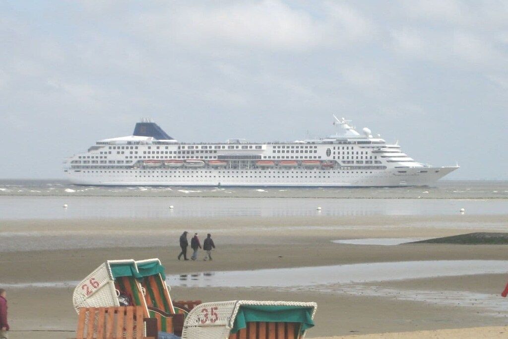 Un grand navire de croisière était amarré sur une plage, et on pouvait apercevoir quelques personnes se promenant au loin.