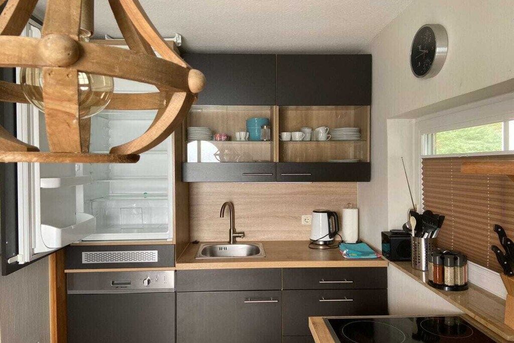 A compact kitchen with a built-in stove, a sink, and a wooden hanging light fixture.