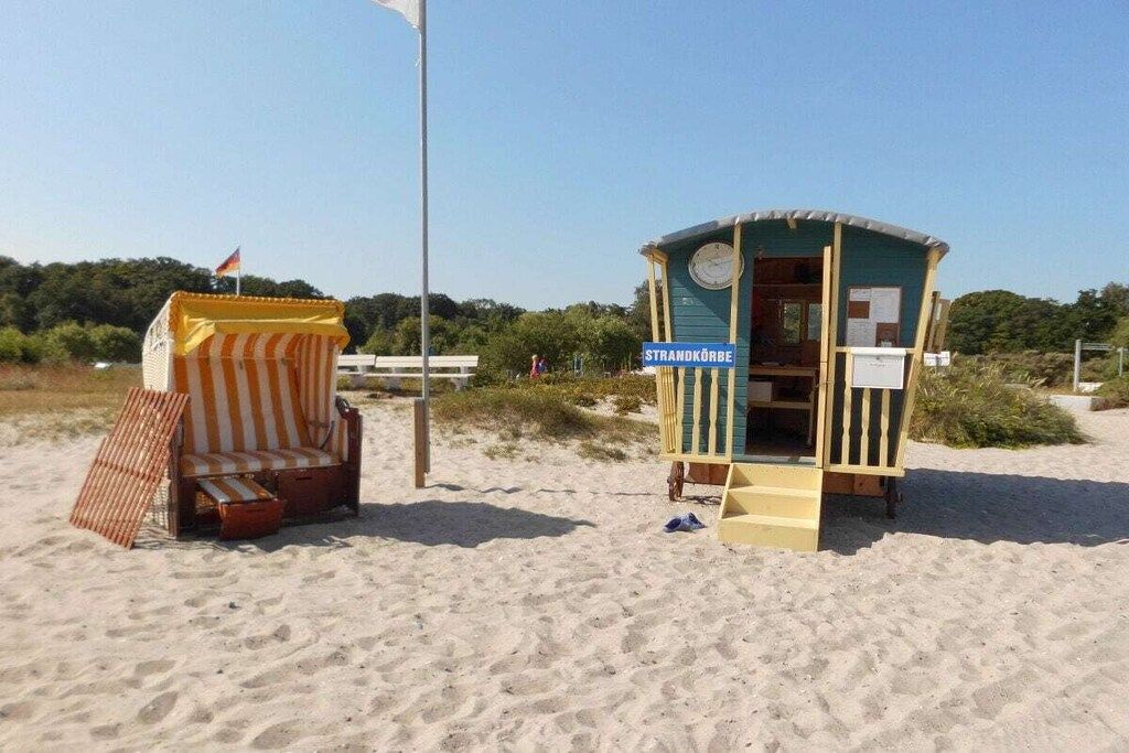 Una cabaña en la playa con un cartel que dice 'STRANDKÖRBE' y una silla de playa a rayas cerca.