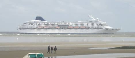 A large cruise ship docked at a beach with a few people walking in the background.
