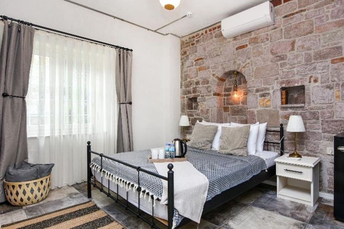 Une chambre avec un mur en pierre, un lit recouvert d’une couvre-lit à motifs, une table de chevet avec une lampe et un petit réfrigérateur.