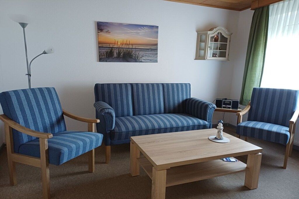 Une pièce comprenant un canapé à rayures, deux fauteuils, une table basse en bois, une lampe, un tableau et un meuble.