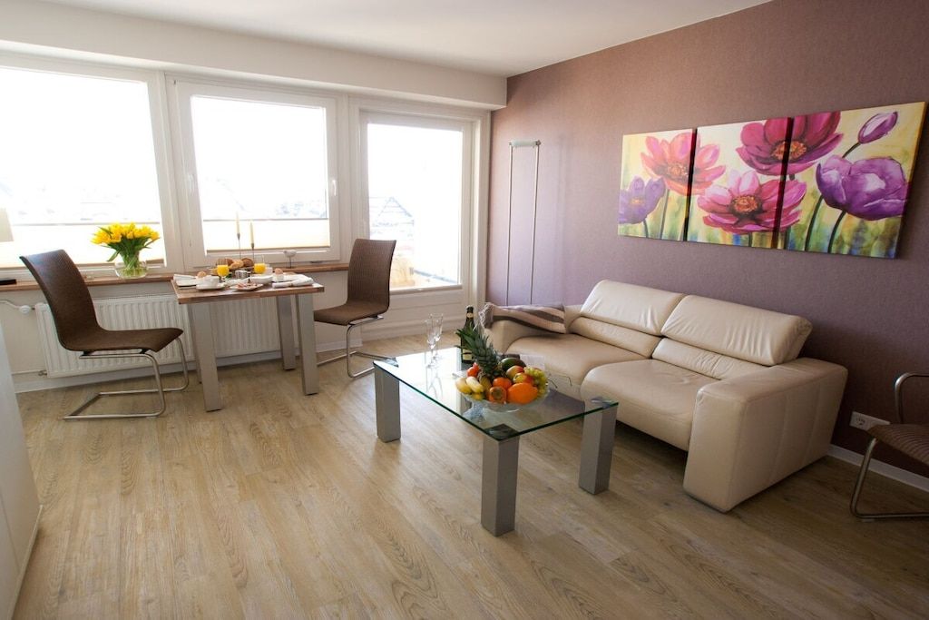 Una sala de estar moderna con una mesa de centro de vidrio, un sofá color beige y un comedor con una mesa dispuesta para el desayuno.