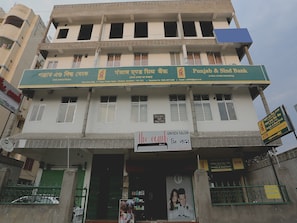 Un edificio de varios pisos con señalización de Punjab & Sind Bank y un salón de belleza unisex.