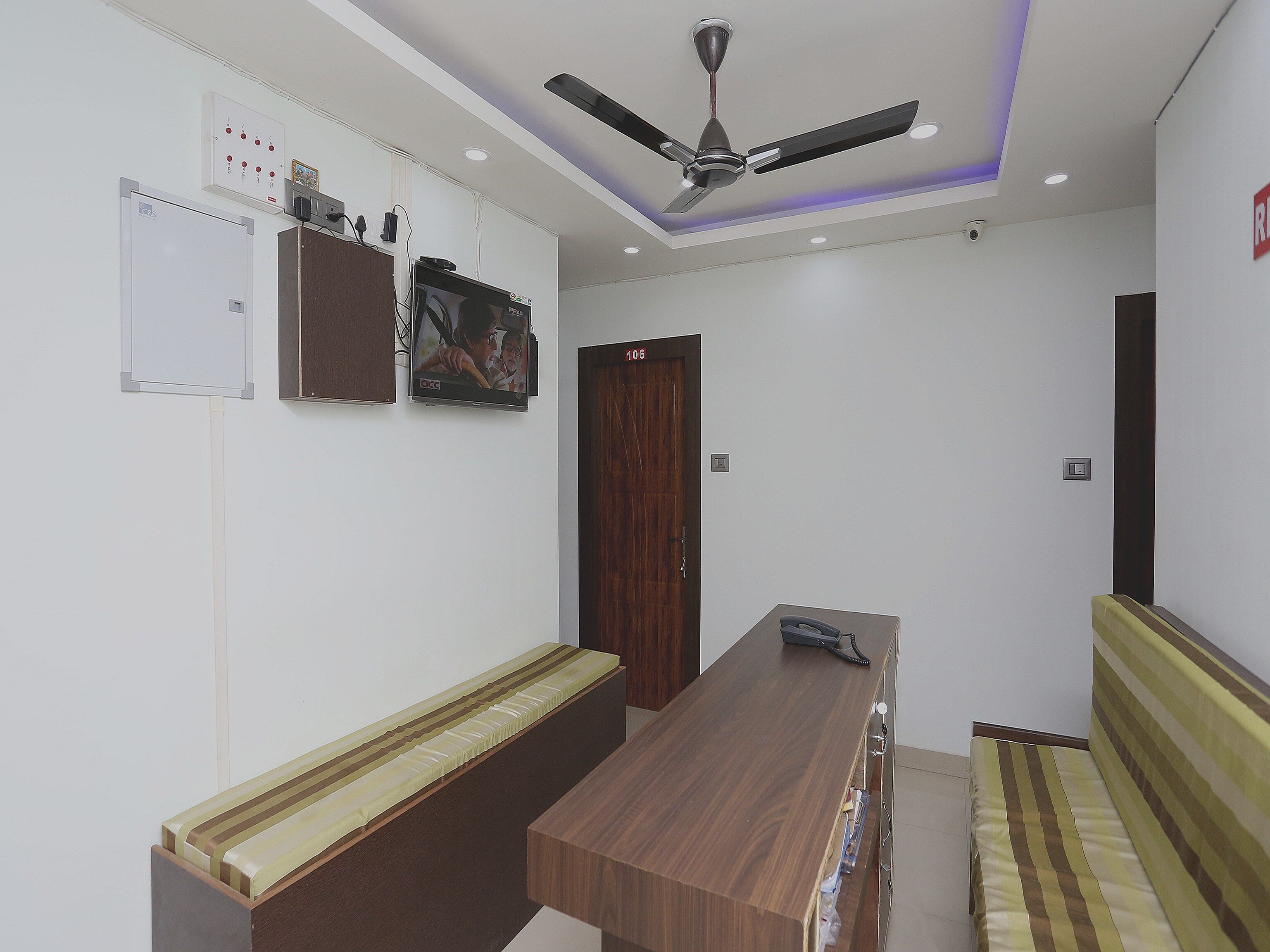 Une pièce dotée d’un ventilateur de plafond, d’un banc en bois, d’un téléviseur fixé au mur et d’une porte portant un numéro.