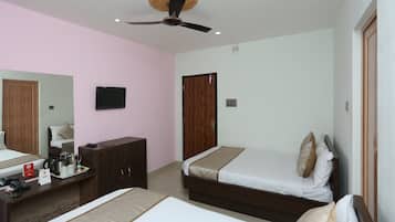 A hotel room with two beds, a desk with a telephone and a coffee maker, a television, and a ceiling fan.