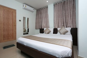 Una habitación de hotel con una cama grande, un armario, un equipo de aire acondicionado y un espejo.