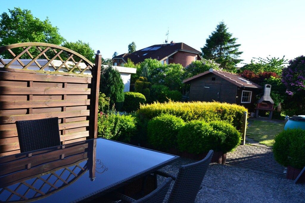 A patio with a table and chairs, surrounded by well-maintained hedges and a brick building.