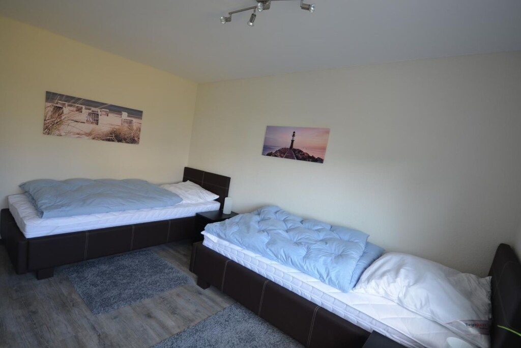 A bedroom with two single beds, a nightstand, a lamp, and two wall-mounted pictures.