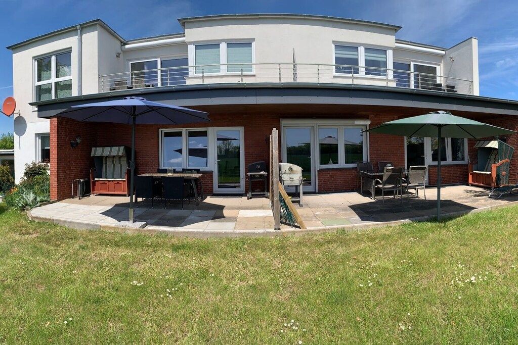 Une maison à deux étages dotée d’un patio comprenant un barbecue, des sièges d’extérieur et des parasols.