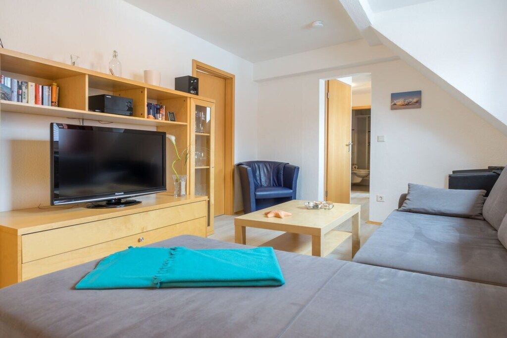 A modern living room with a flat-screen TV, a sofa, a coffee table, and a bookshelf.