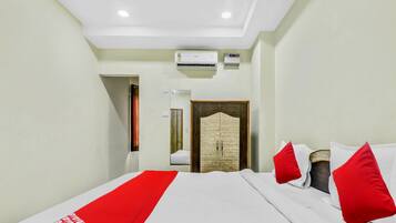 A hotel room with a bed, a wardrobe, an air conditioning unit, and a door.