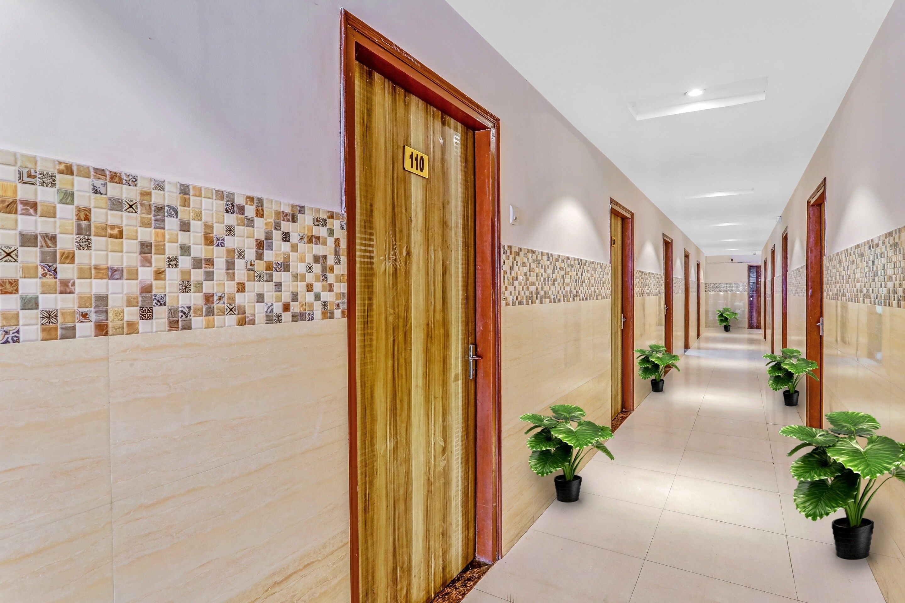 A hotel corridor with tiled walls, wooden doors, and potted plants.