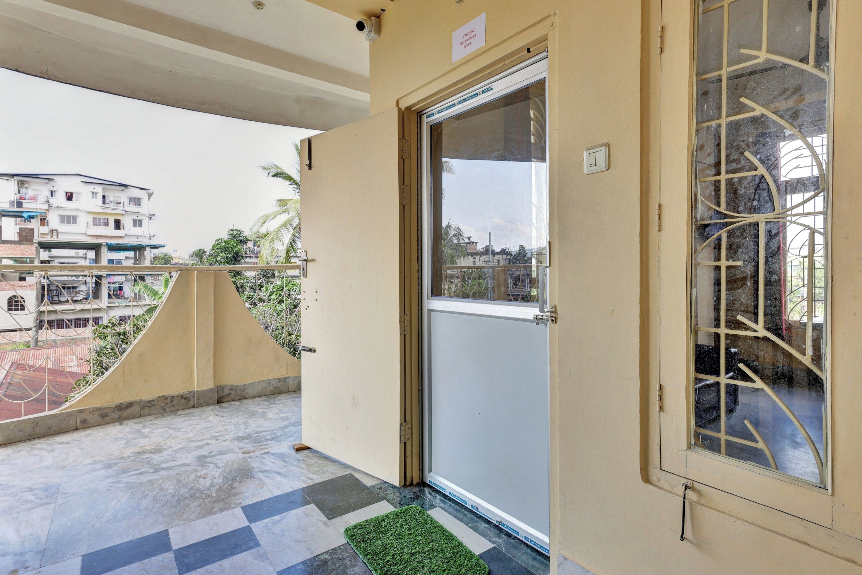 Un balcón con una puerta, una ventana con rejas y vistas a edificios al fondo.