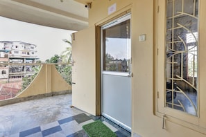 Un balcón con una puerta, una ventana con rejas y vistas a edificios al fondo.