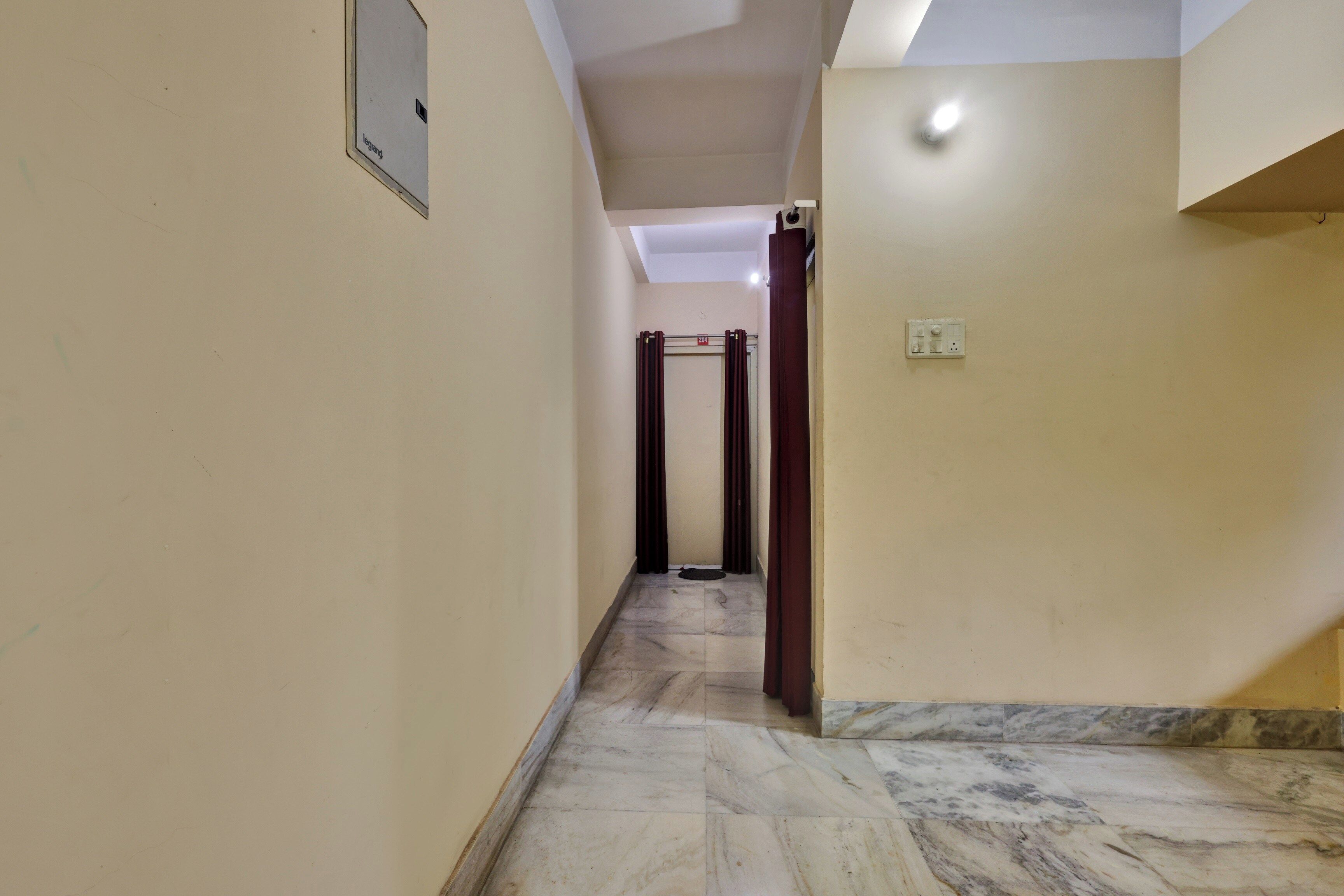 Un pasillo con piso de mármol, una puerta con el símbolo de número y una lámpara en la pared.
