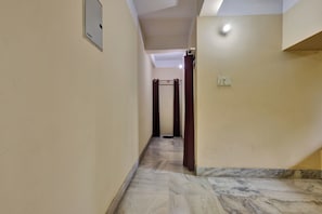 Un pasillo con piso de mármol, una puerta con el símbolo de número y una lámpara en la pared.