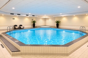 Ein rechteckiger, überdachter Schwimmteich mit klarem, blauem Wasser, umgeben von beige gefliesten Wänden und einer Decke mit eingelassener Beleuchtung.