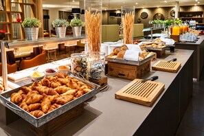 En buffet med et udvalg af mad, blandt andet kager og brød, i et moderne hotelmiljø.