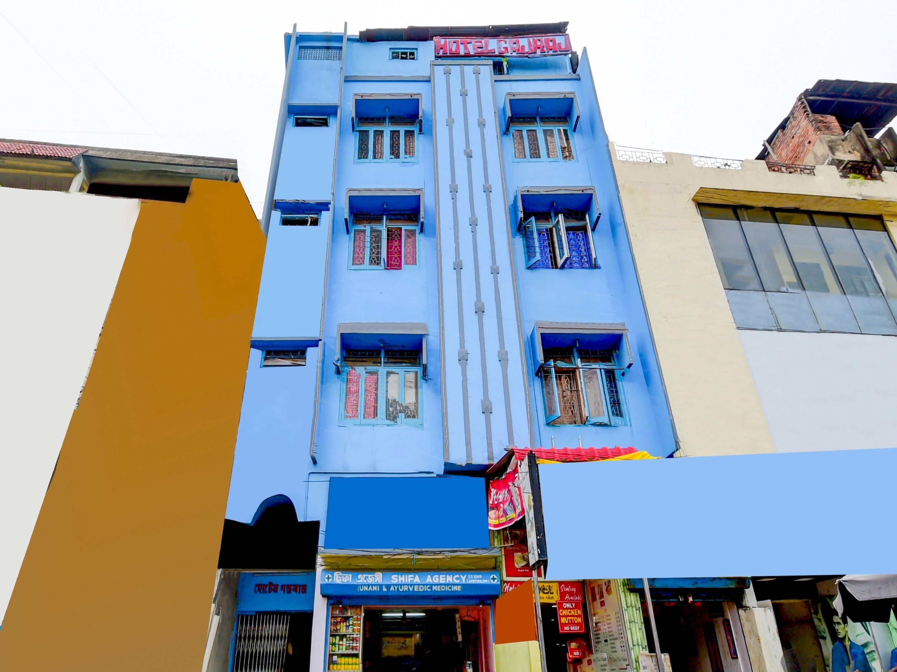 A multi-story building with a blue facade, a sign for a hotel, and a pharmacy at the ground level.