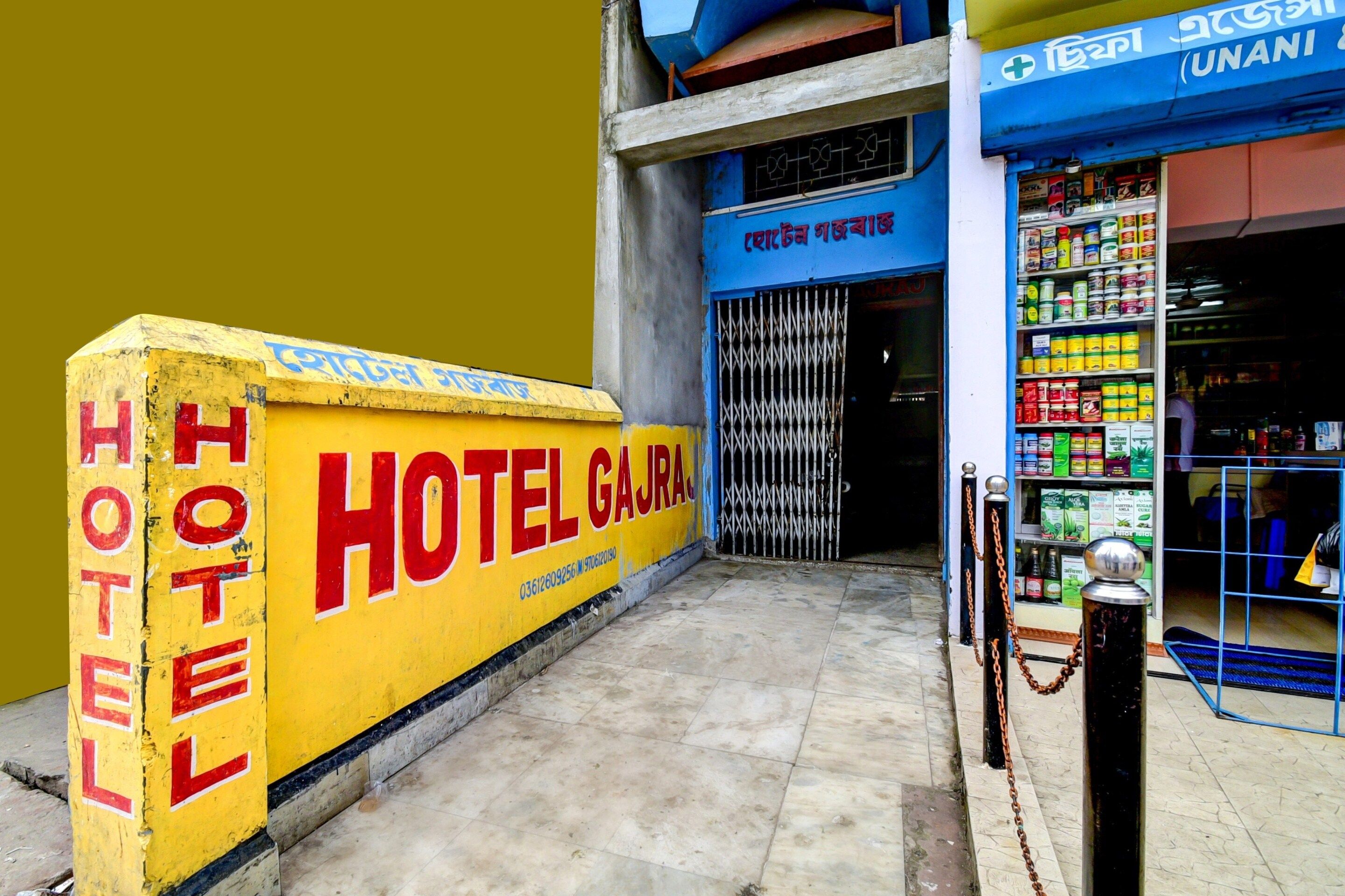 A hotel entrance with a yellow sign, a metal gate, and a pharmacy across the street.