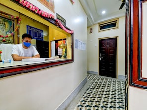 A hotel reception desk with a man seated behind it, a check-out time sign, and a framed picture above the desk. - Hotel O Gajraj (Guwahati)