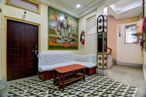 A room with a wooden door, a white sofa, a patterned floor, a wall with a religious painting, and a fire extinguisher. - Hotel O Gajraj (Guwahati)