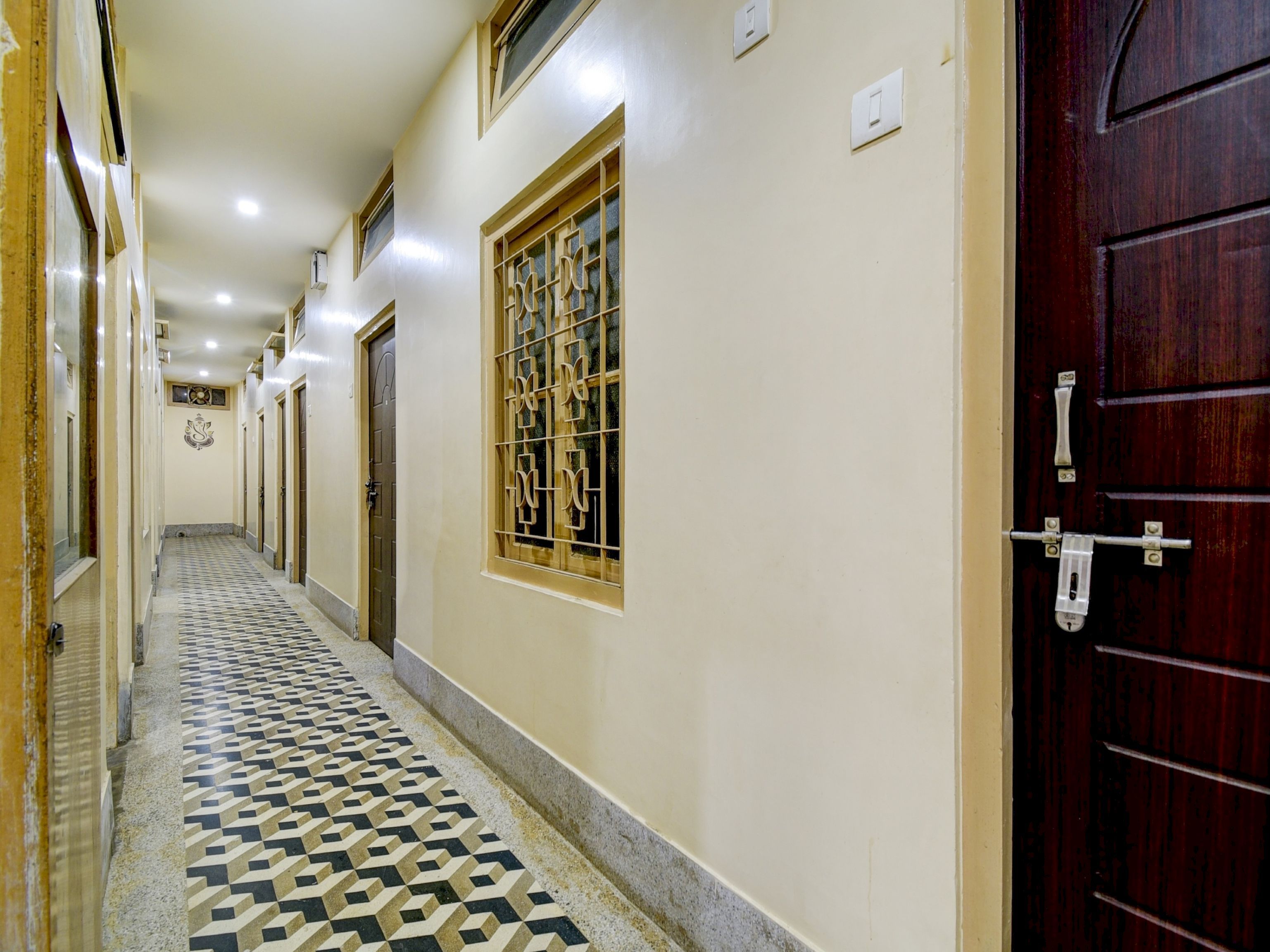 A corridor with patterned flooring, a wooden door with a metal handle, and a window with decorative bars.